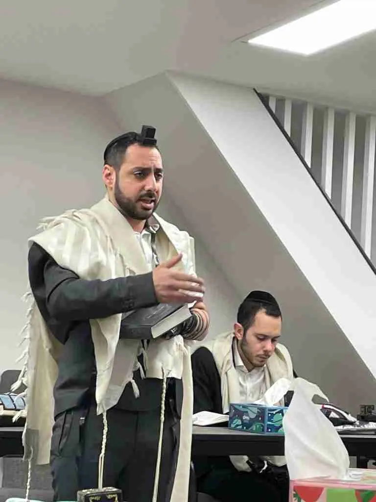 A rebbi in tallit and tefillin giving a morning shiur at the Brooklyn program