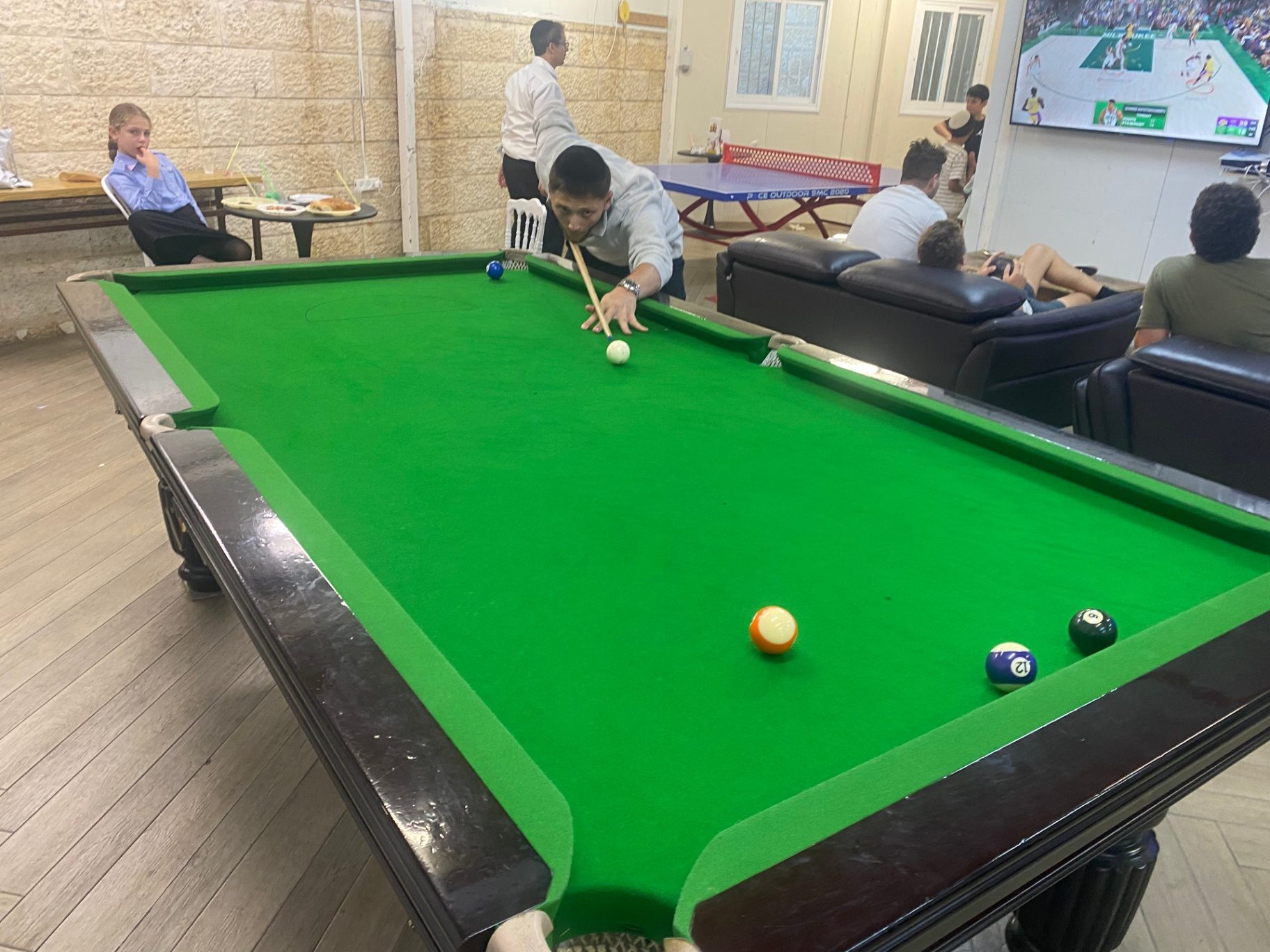 A talmid taking a shot at the pool table in the game room