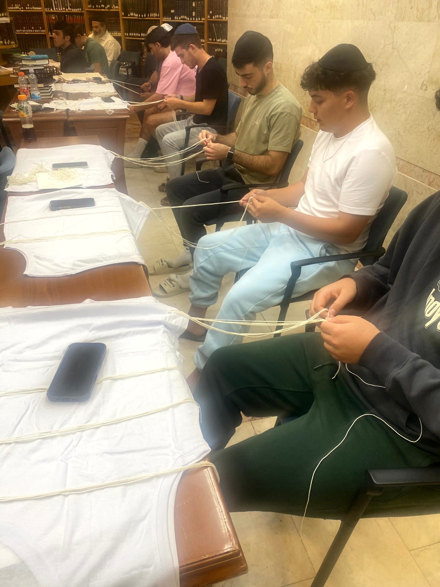 Talmidim seated together tying tzitzit onto tallitot